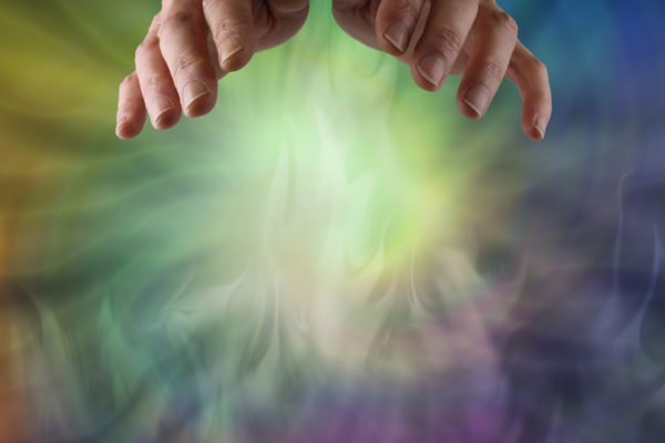 female hands hovering over a wispy spiral of multicoloured ethereal energy  with plenty of copy space